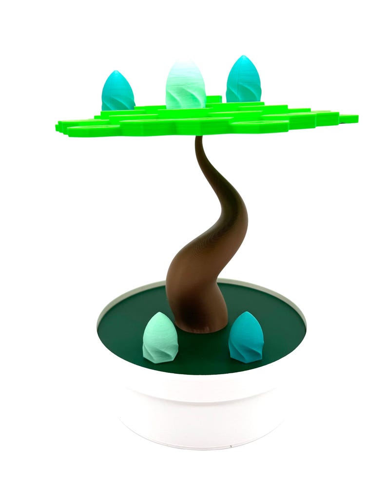 May include: A decorative tree sculpture with a brown trunk, green leaves, and teal-colored egg-shaped accents. The tree sits in a white pot with a dark green base. The sculpture is a modern, abstract design.