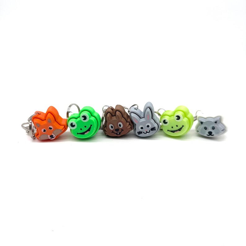 May include: A set of six colorful plastic animal-shaped stitch markers. The markers feature a fox, frog, hedgehog, bunny, frog, and wolf.