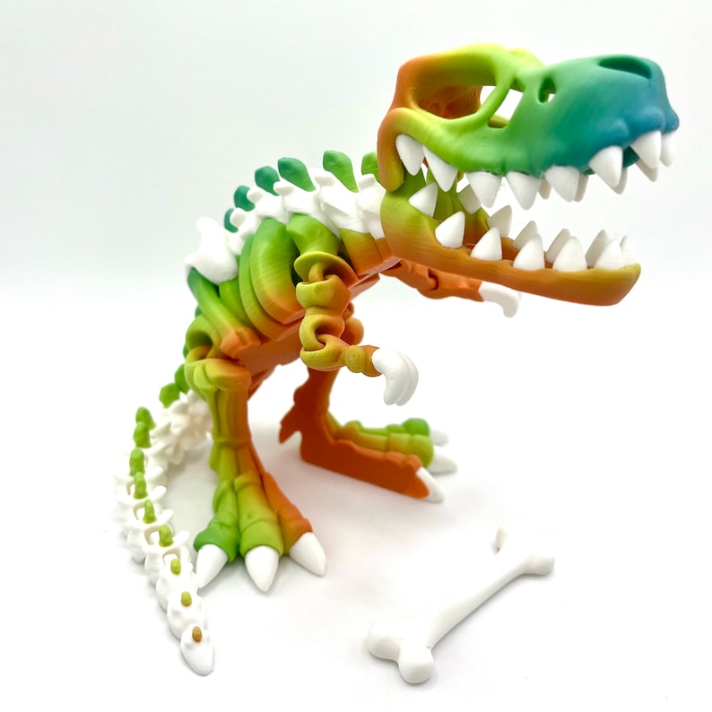 May include: A colorful, articulated dinosaur skeleton toy with a gradient of green, yellow, and orange. The dinosaur is posed in a standing position with its mouth open, revealing white teeth. The toy is made of plastic and has a white bone accessory.