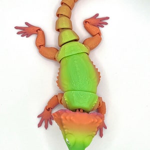May include: A green, orange, and red articulated toy lizard with a spiky head and a long tail.