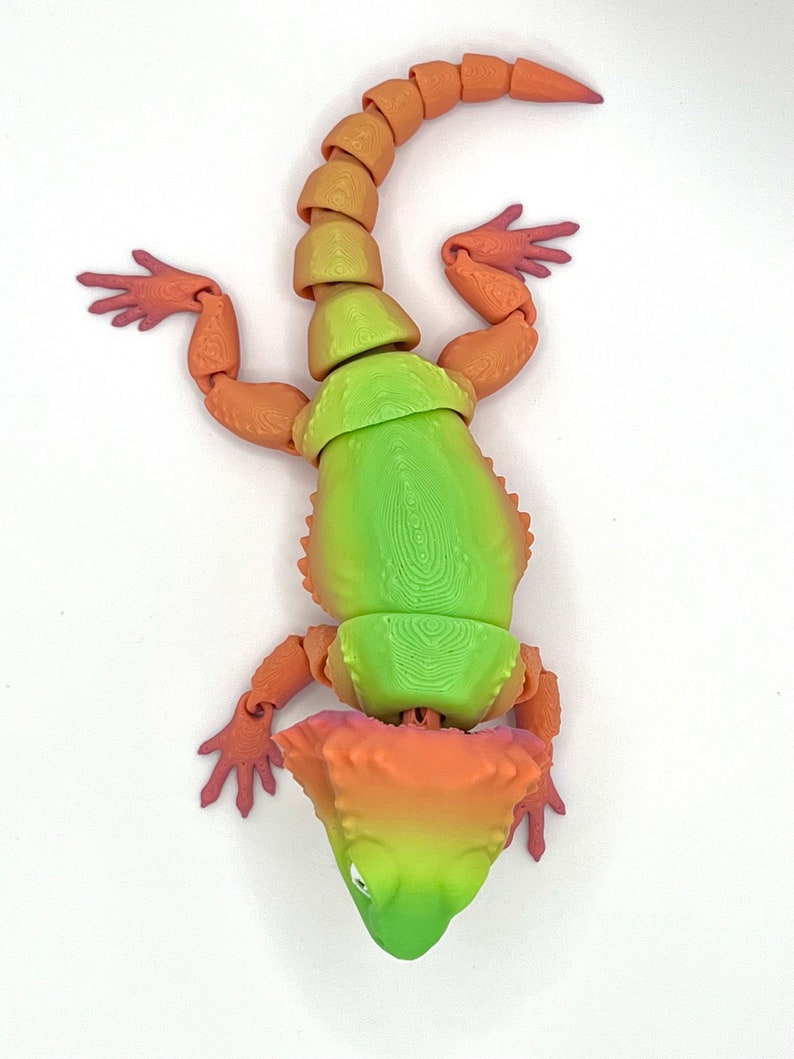 May include: A green, orange, and red articulated toy lizard with a spiky head and a long tail.