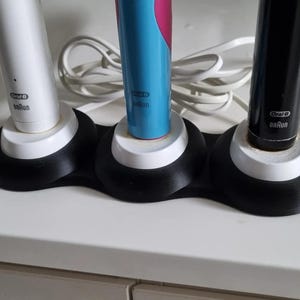 May include: A black charging station with three white charging bases for electric toothbrushes. The toothbrushes are white, blue, and black with the Oral-B brand name on each.
