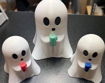 May include: Three white ghost-shaped figurines holding small cups in their hands. The cups are different colors: green, red, and blue.