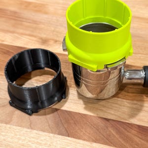 May include: A black and a bright green 3D printed coffee tamper accessory for a portafilter. The black accessory is a ring that fits around the portafilter. The green accessory is a ring that fits around the top of the portafilter.