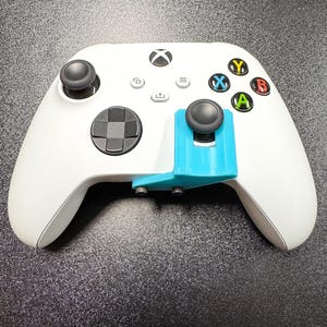 May include: A white Xbox controller with black joysticks and colored buttons. A light blue accessory is attached to the controller. The text "© Kleet3DPrints" is visible in the bottom left corner.