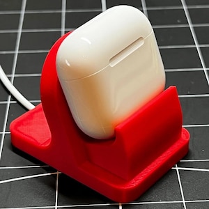 May include: A red 3D printed stand for wireless charging a white AirPod case.