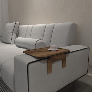 May include: A white sofa with black trim and a wooden tray attached to the armrest. A white cup and saucer are on the tray.