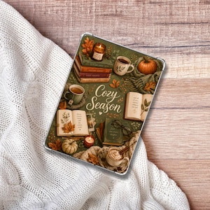 May include: A rectangular tablet case featuring a printed illustration of autumn-themed items including stacked books, a pumpkin, mugs of coffee, a lit candle, and eyeglasses. The text "Cozy Season" is printed in the center in a script font.