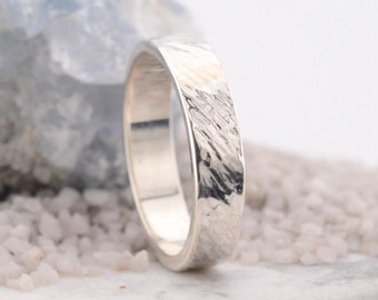 May include: A silver ring with a textured, hammered finish. The ring is wide and has a polished interior.