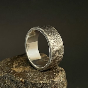 Op de afbeelding: Een zilveren ring met een getextureerde, gehammerde afwerking. De ring is breed en heeft een afgeronde rand.