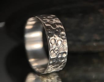 May include: A silver ring with a hammered texture. The ring is wide and has a rounded band.