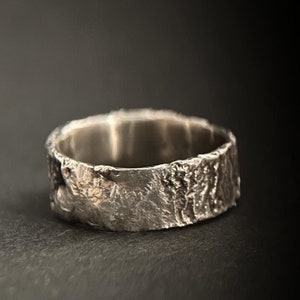 Könnte beinhalten: Ein silberner Ring mit einem strukturierten, rindenartigen Design. Der Ring ist breit und hat eine glatte Innenfläche.