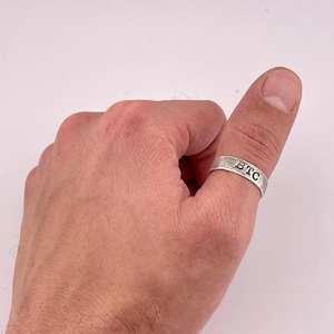 Könnte beinhalten: Ein silberner Daumenring mit den eingravierten Buchstaben "BTC".
