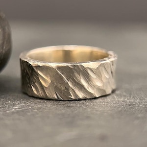 Op de afbeelding: Een zilveren ring met een getextureerde, gehammerde afwerking. De ring is breed en heeft een afgeronde vorm.
