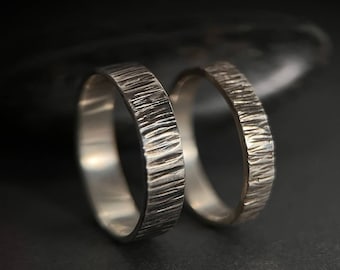 May include: Two silver wedding bands with a textured, hammered finish. The bands are stacked on top of each other.