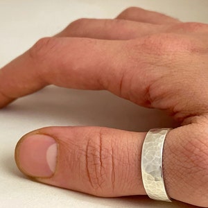 Könnte beinhalten: Ein silberner, gehämmerter Daumenring. Der Ring ist breit und hat eine strukturierte Oberfläche.