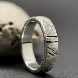 Puede incluir: Un anillo de plata con un acabado texturizado martillado y una serie de líneas verticales grabadas en la banda.