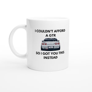 Könnte beinhalten: Weiße Keramik-Tasse mit einer schwarzen Auto-Illustration und dem Text: "I COULDN'T AFFORD A GTR SO I GOT YOU THIS INSTEAD."