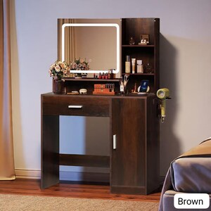 May include: A brown vanity with a lighted mirror, a drawer, and a cabinet. The vanity has a shelf with beauty products and a space for a phone. A hairdryer hangs on the side. The vanity is designed for makeup and beauty routines.