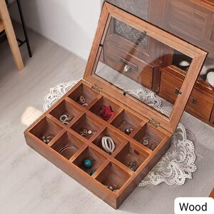 May include: A wooden jewelry box with a glass lid, divided into multiple compartments. The box is filled with various rings, earrings, and other small jewelry items. The box is made of wood and has a warm, brown tone.
