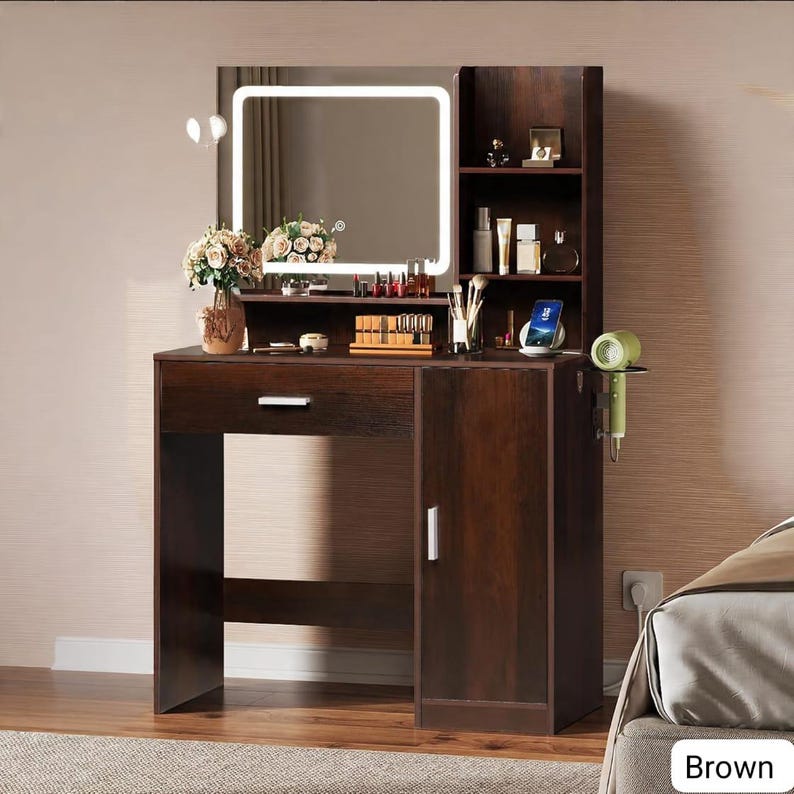 May include: A brown vanity with a lighted mirror, a drawer, and a cabinet. The vanity has shelves for storage and a small shelf for a hair dryer. The mirror is square with a white light border. The vanity is in a bedroom.