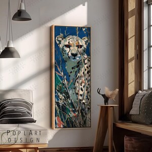 Könnte beinhalten: Gerahmter, vertikaler Kunstdruck mit einem Geparden. Der Gepard hat ein geflecktes Fell und ist vor einem blauen Hintergrund mit grünem und braunem Laub abgebildet. Das Kunstwerk befindet sich in einem Holzrahmen.