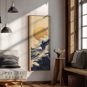 Könnte beinhalten: Gerahmter Wandkunstdruck mit einer stilisierten Darstellung einer großen Meereswelle mit untergehender Sonne. Das Kunstwerk ist in Blau-, Weiß- und Goldtönen gehalten und hat einen Holzrahmen. Der Druck wird in einem hellen Raum gezeigt.