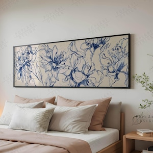 Op de afbeelding: Een groot, ingelijst kunstwerk met blauwe lijntekeningen van bloemen op een beige achtergrond hangt boven een bed. Het bed heeft een houten frame, witte lakens en een roze sprei. Decoratieve kussens in verschillende tinten wit en roze maken de slaapkamer compleet.