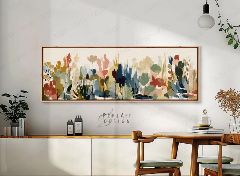 May include: Abstract floral painting in a rectangular wooden frame. The artwork features a variety of colorful, stylized flowers and foliage in shades of red, blue, green, and beige. The painting is displayed above a white cabinet and wooden table.