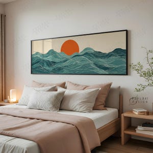 Könnte beinhalten: Ein gerahmter Wandkunstdruck mit einer orangefarbenen Sonne, die über türkisfarbenen Meereswellen untergeht. Das Kunstwerk wird über einem Bett mit hellem Holzrahmen, einem rosa Bettbezug und verschiedenen Kissen gezeigt. Der Raum hat eine neutrale Farbpalette.