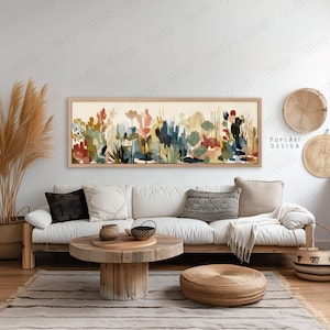 May include: A long, rectangular framed artwork featuring an abstract floral design in shades of red, blue, green, and beige. The artwork hangs above a white sofa with decorative pillows. A woven basket and decorative trays are also visible.
