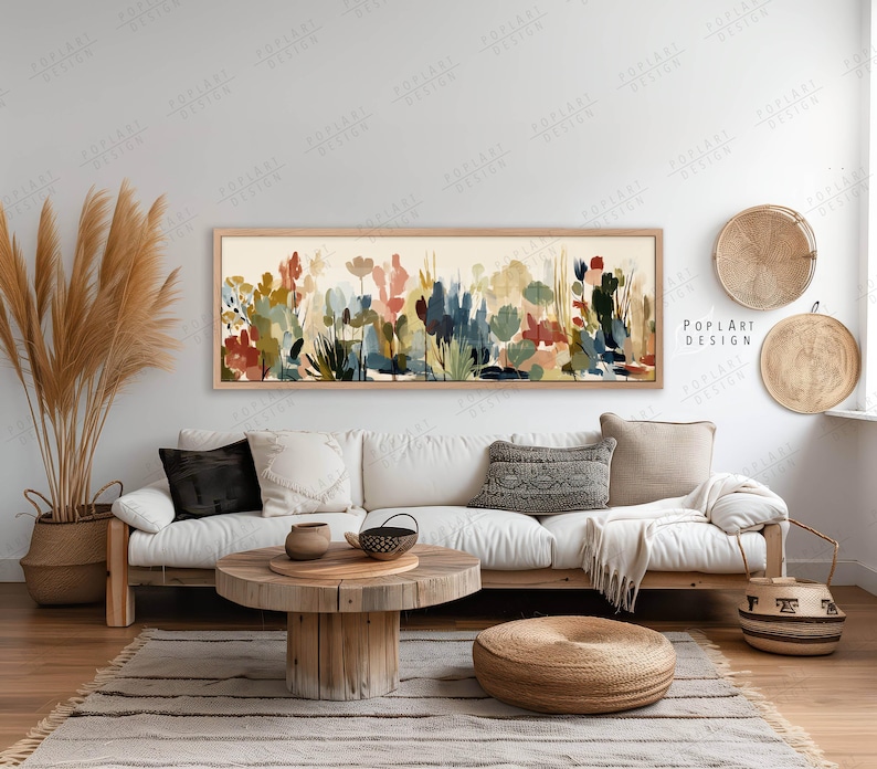 May include: A long, rectangular framed artwork featuring an abstract floral design in shades of red, blue, green, and beige. The artwork hangs above a white sofa with decorative pillows. A woven basket and decorative trays are also visible.
