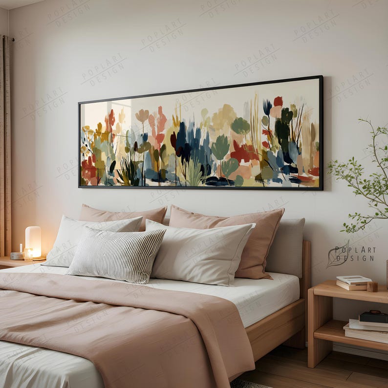 May include: A framed abstract art piece with a black border hangs above a bed. The artwork features colorful brushstrokes in shades of red, blue, green, and yellow. The bed has a wooden frame, white sheets, and various pillows.
