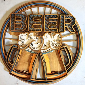 May include: A wooden wall decor with the word "BEER" in a wavy font. The design features two beer mugs with foam on top, surrounded by a blue and orange circle with a sunburst pattern.