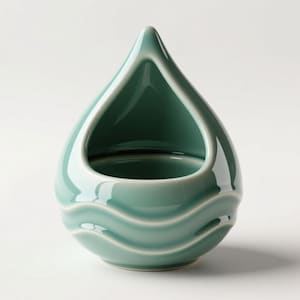 Peut inclure: Un bol décoratif en céramique de couleur sarcelle en forme de goutte d'eau. Le bol a une finition lisse et brillante avec un bord blanc et trois crêtes en forme de vagues à la base. L'ouverture est triangulaire.