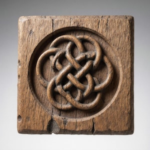 May include: A square, weathered wooden carving featuring a Celtic knot design within a circular frame. The wood has a natural, aged appearance with visible grain and cracks, showcasing a rustic aesthetic. The knotwork is intricately carved.