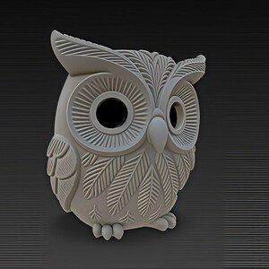 May include: A light gray owl figurine with detailed feather and eye designs. The owl has large, round eyes and a textured surface. The figurine is set against a dark gray background with horizontal lines.