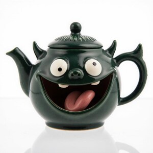 May include: A whimsical, dark green ceramic teapot with a cartoonish monster face. The teapot features large white eyes, a wide open mouth with a pink tongue, and small horns. The lid has a small knob.