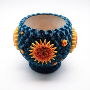 Puede incluir: Un cuenco decorativo hecho a mano con un exterior azul oscuro adornado con diseños de papel en espiral. El cuenco presenta detalles de sol y flores amarillas y naranjas. El interior es de color beige claro. El cuenco tiene unos 13 cm de diámetro.