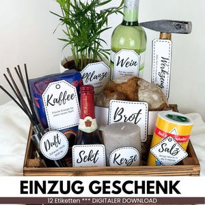 Op de afbeelding: Een houten dienblad gevuld met diverse items, waaronder een fles wijn, een kleine plant, een brood, een kaars en een zoutpot. Elk item heeft een label. Het dienblad heeft de tekst "EINZUG GESCHENK" en "12 Etiketten *** DIGITALER DOWNLOAD".