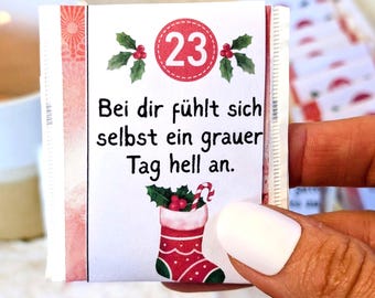 May include: A small, white packet with a red and white border, featuring the number 23 in a red circle, holly, and the text "Bei dir fühlt sich selbst ein grauer Tag hell an." A Christmas stocking illustration is also present.