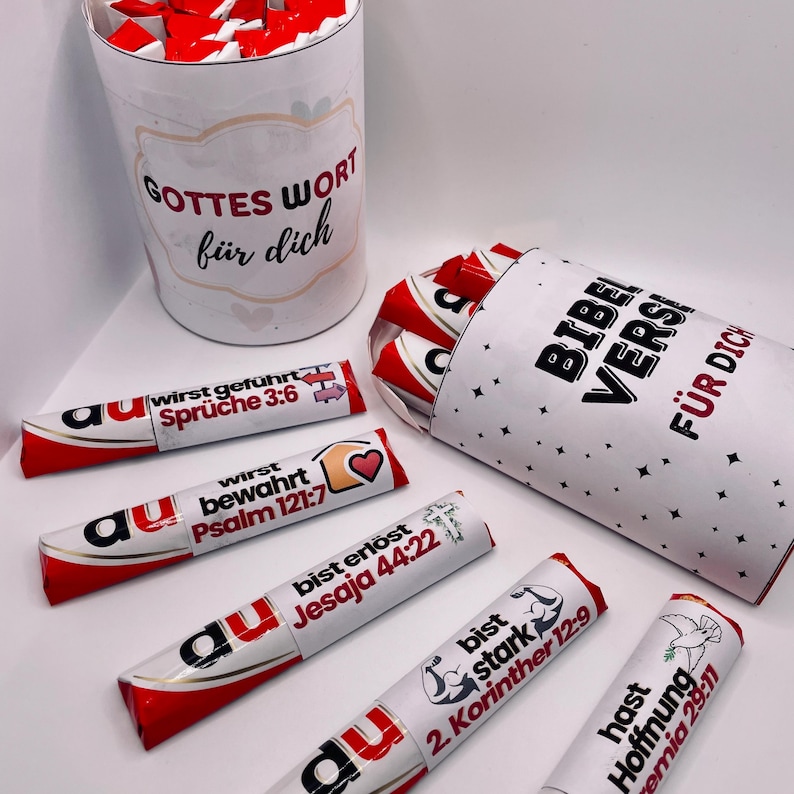 May include: A set of small chocolate bars wrapped in red and white foil with inspirational Bible verses printed on the wrappers. The bars are arranged in two white cardboard tubes with black text that reads "Gottes Wort f&uuml;r dich" and "Bibel Verse f&uuml;r dich".
