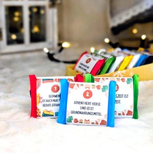 May include: Advent calendar with numbered packages in red, blue, and green. The packages have text in German, with festive illustrations of gingerbread houses and gifts. A yellow box holds additional packages.