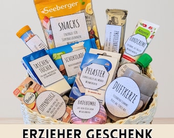 May include: A gift basket filled with various items, including snacks, chocolate, bandages, hand cream, and a bath bomb. The basket contains several products with labels in German, and the text "ERZIEHER GESCHENK" is displayed at the bottom.