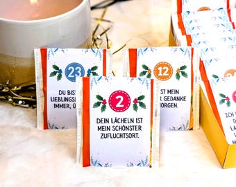 May include: Advent calendar with numbered packets. Each packet has a white background with a blue and red border, and a sprig of holly. The packets have German text, including "Dein Lächeln ist mein schönster Zufluchtsort."