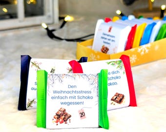 Op de afbeelding: Adventskalender met chocoladerepen. Elke reep is verpakt in wit papier met gekleurde randen en linten. De repen hebben tekst en illustraties van chocolade. De kalender zit in een gele doos met sneeuwvlokken.
