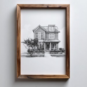 Może przedstawiać: Oprawiony czarno-biały szkic dwupiętrowego domu z werandą, lukarną i krajobrazem. Grafika znajduje się w rustykalnej brązowej drewnianej ramie, zamontowanej na białej ścianie. Dom ma wiele okien i drzwi wejściowe.