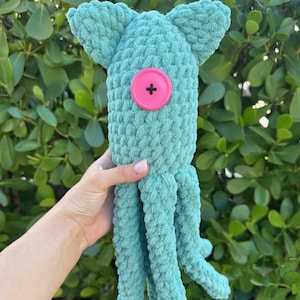 May include: A teal blue crocheted octopus plush toy with a pink button for an eye.