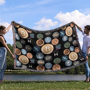 May include: A black woven throw blanket with a repeating pattern of various cryptocurrency logos and symbols, including Bitcoin, Ethereum, Dogecoin, and Shiba Inu. The blanket is being held up by two people.