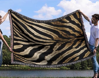 Könnte beinhalten: Eine gewebte Wolldecke mit Zebra-Muster in Braun-, Schwarz- und Weißtönen. Die Decke wird von zwei Personen gehalten.